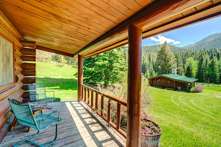 Log cabin porch with two green chairs looking out over green grass at second log cabin